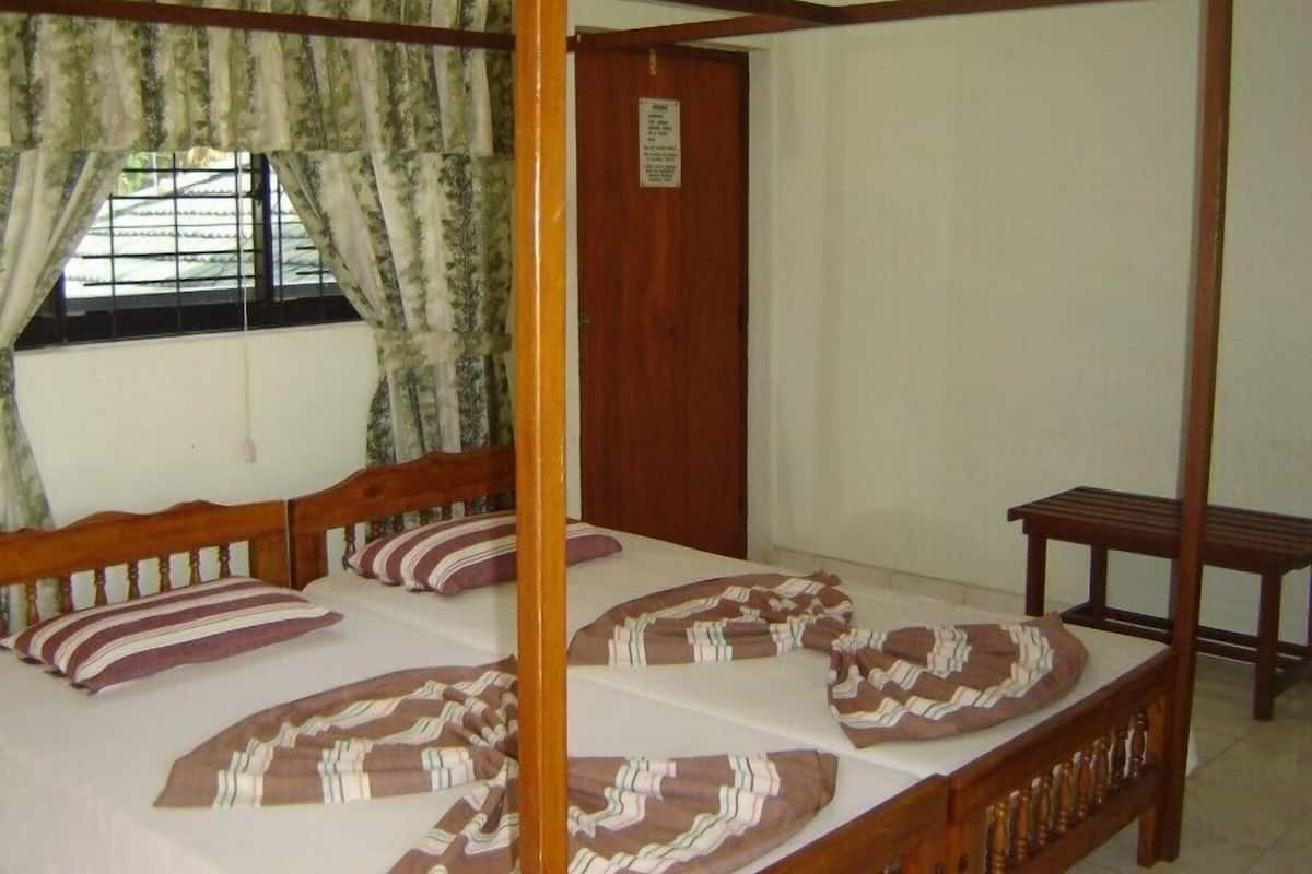 A four-poster bed with striped bedding, a wooden bench, and a window with curtains.
