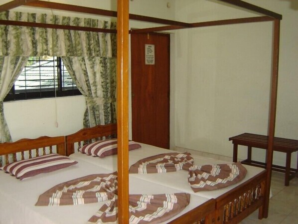 A four-poster bed with striped bedding, a wooden bench, and a window with curtains. - Ocean View Guesthouse (Negombo)
