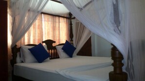 A bed with white bedding and blue pillows, a wooden headboard, and a canopy with sheer curtains. - Ocean View Guesthouse (Negombo)