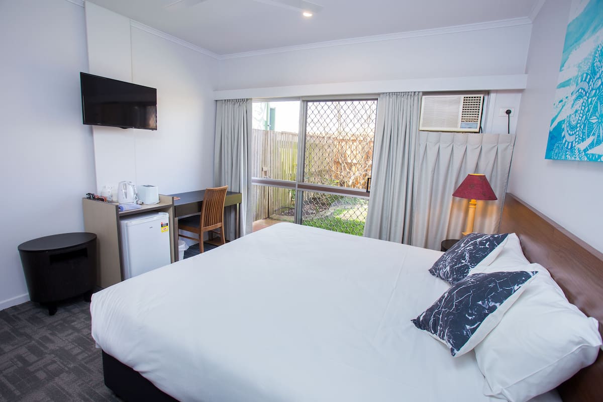 A hotel room with a bed, a desk, a chair, a TV, and a window with curtains.
