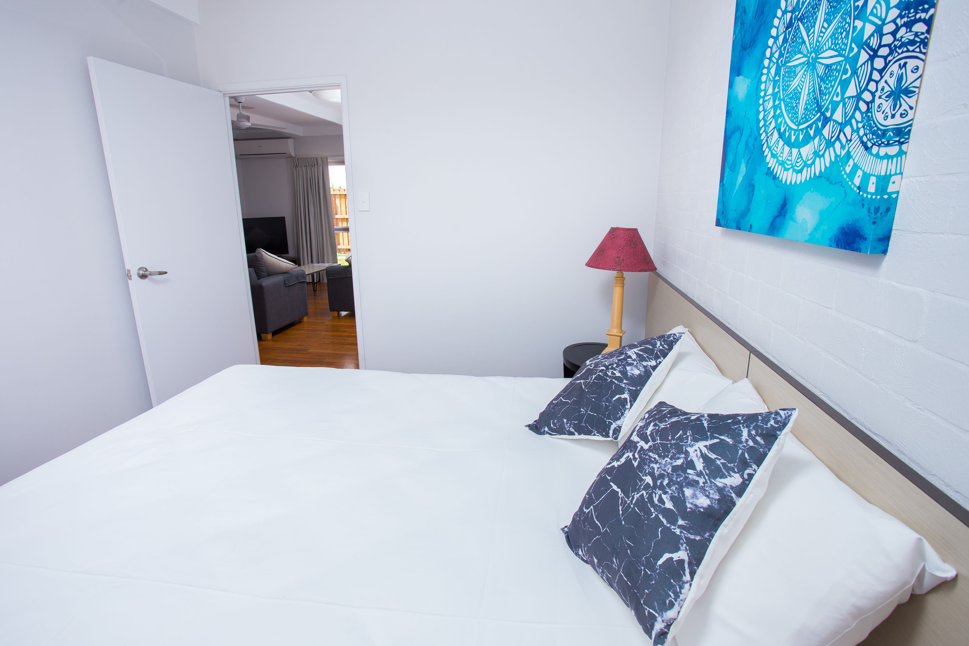 Quarto com cama, travesseiros, luminária e uma obra de arte na parede.