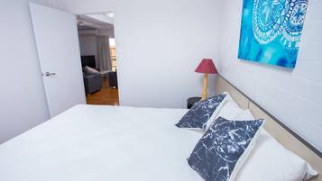 Quarto com cama, travesseiros, luminária e uma obra de arte na parede.