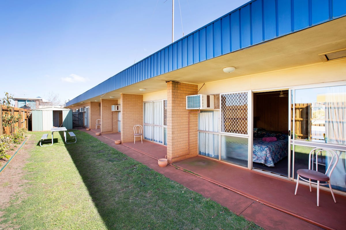 A motel with a patio area, a small garden, and a room with a bed and window.