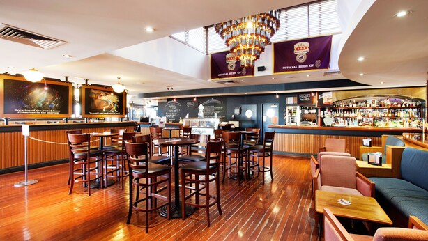 A bar area with wooden flooring, bar stools, and a high ceiling with a chandelier. - Wilsonton Hotel (Wilsonton)
