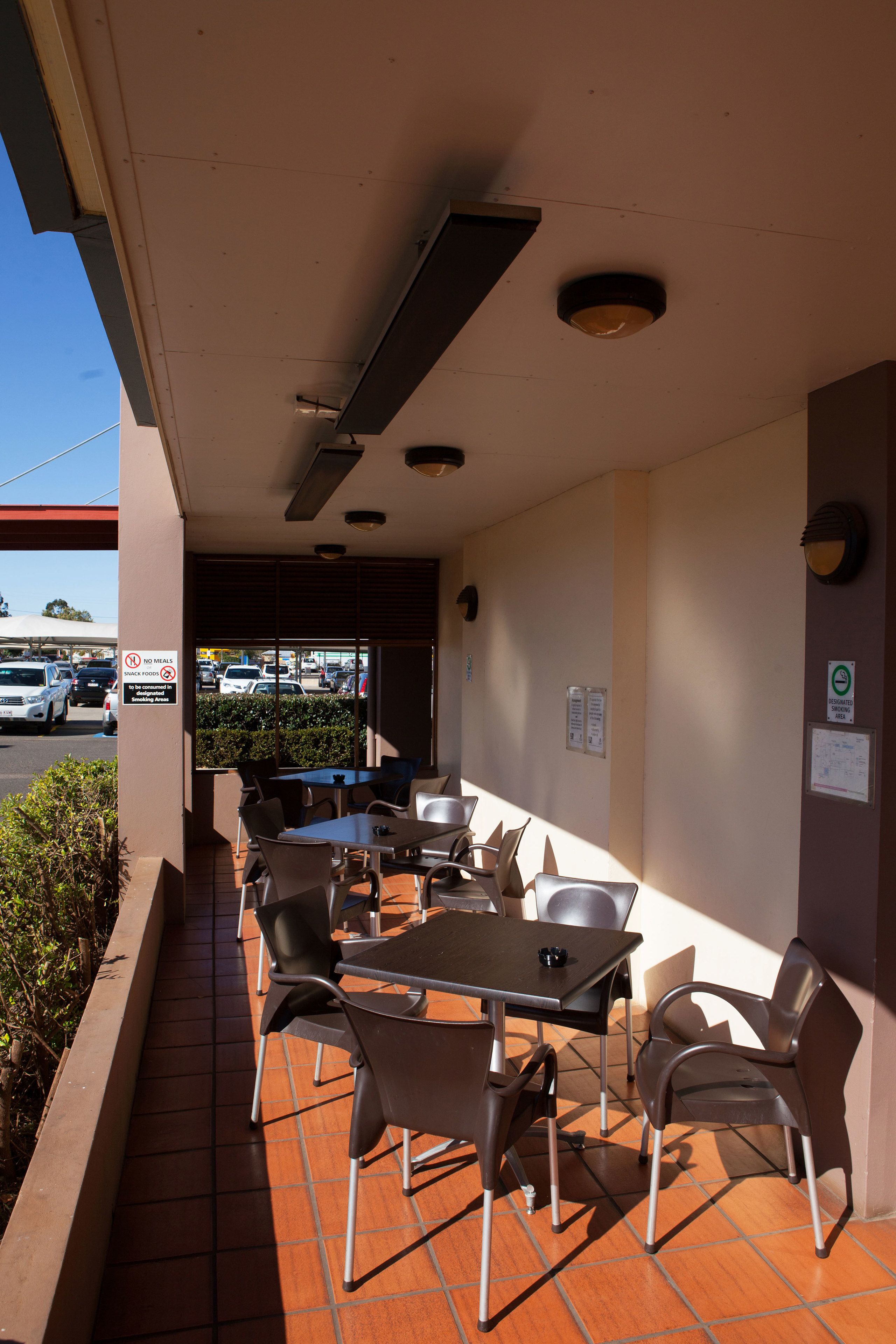 An outdoor cafe area with tables and chairs, a tiled floor, and a view of the street with parked cars.
