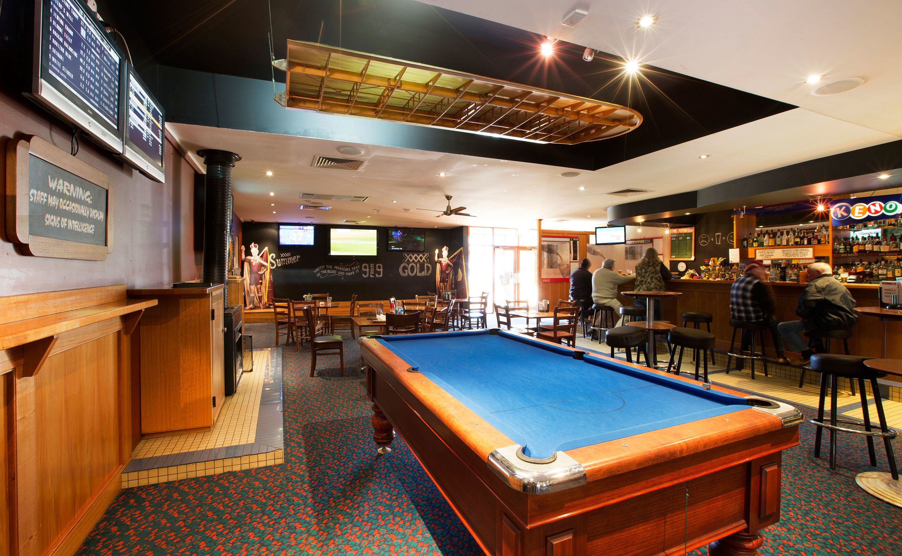 Una mesa de billar en un área de bar con muebles de madera y una barra.