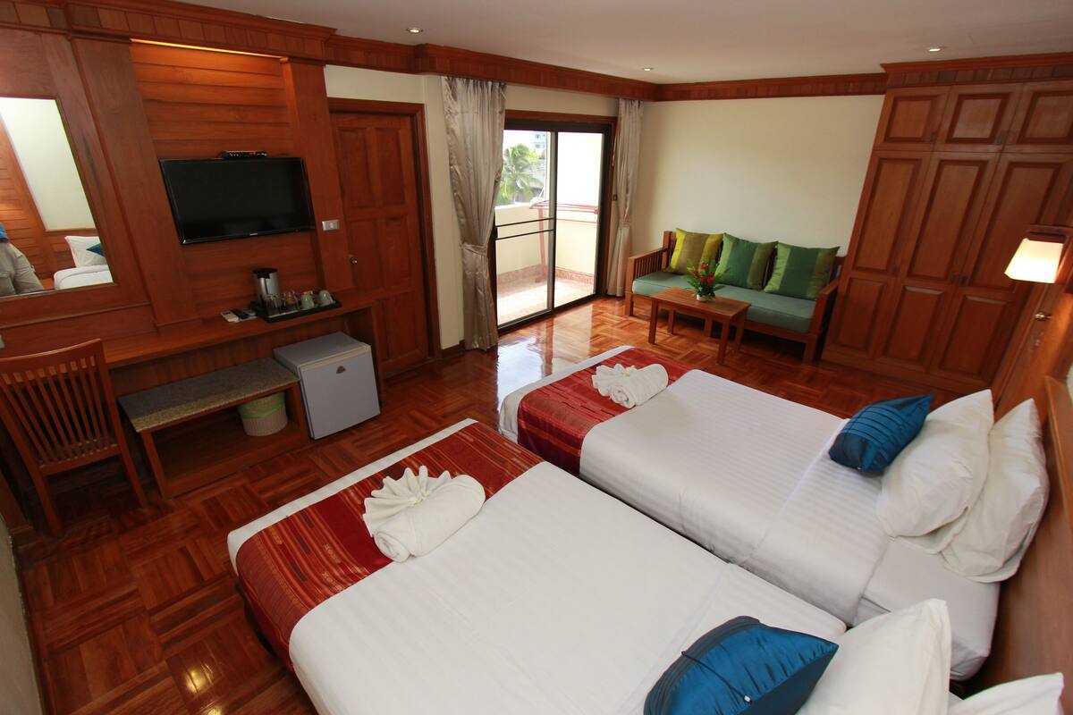 Une chambre d’hôtel avec deux lits, une télévision, un bureau, une chaise, une petite table et un canapé.
