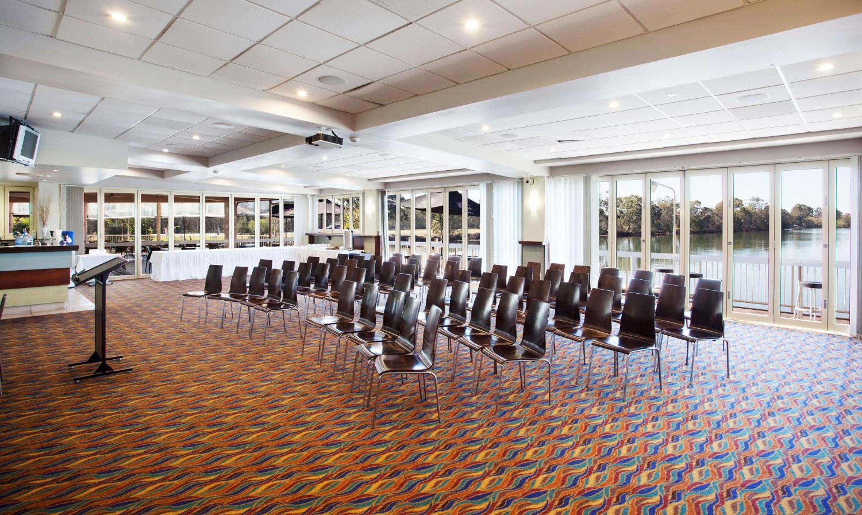 Une salle de conférence avec des rangées de chaises, un pupitre et une grande fenêtre donnant sur une étendue d’eau.