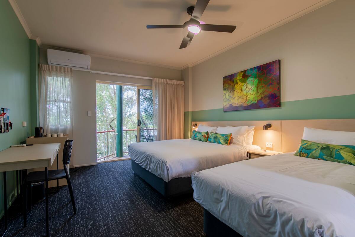 Ein Hotelzimmer mit zwei Betten, einem Schreibtisch und einem Deckenventilator.
