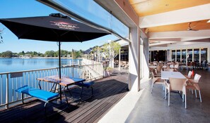 Terraza exterior con mesas y sillas, con vista a un cuerpo de agua.