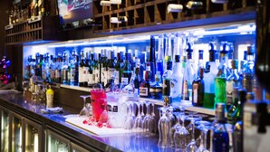 Una zona de bar con una variedad de botellas y copas, una pantalla de televisión y una sección refrigerada.