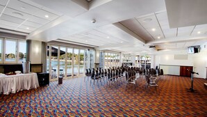 Un salón de conferencias con filas de sillas, un escenario con un atril y amplias ventanas con vistas a un cuerpo de agua.