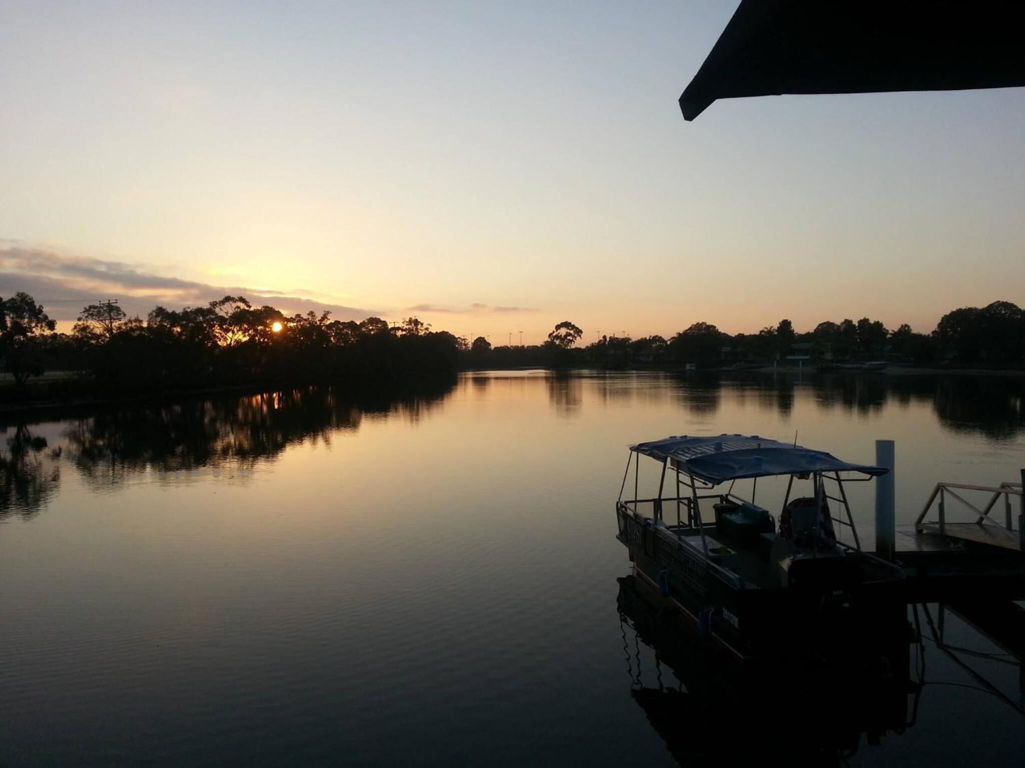 A calm lake at sunset with a boat docked on the right.