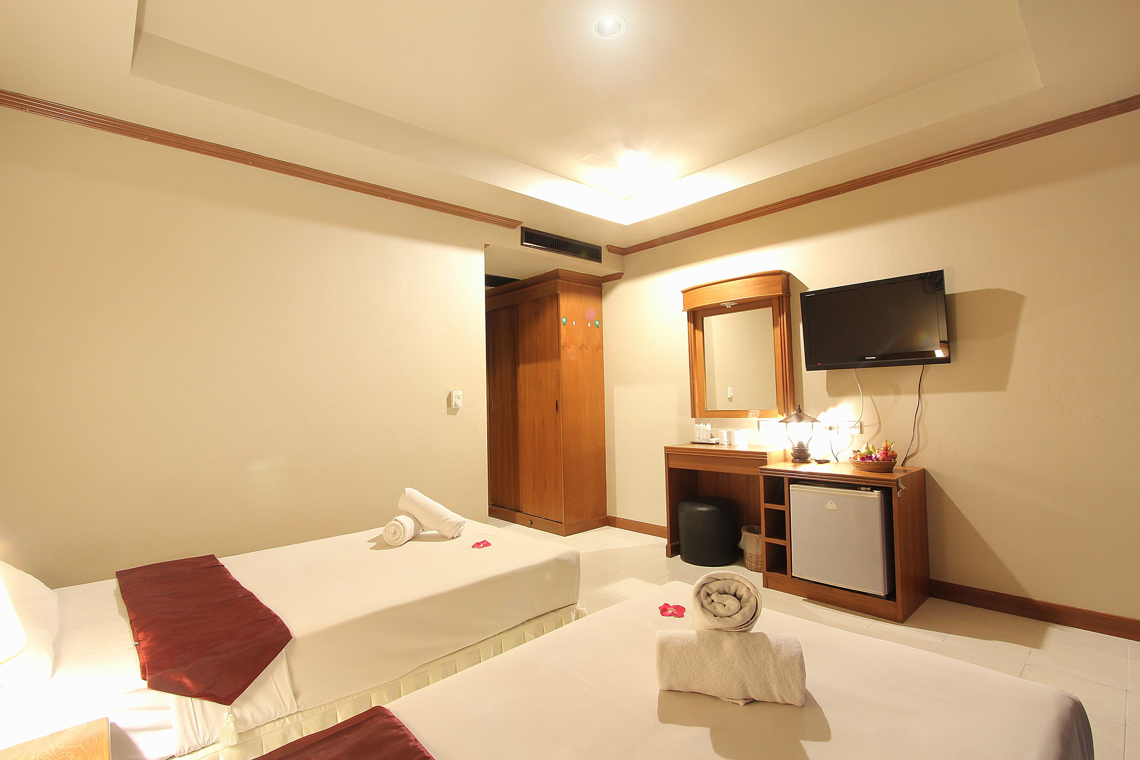 A hotel room with two beds, a television, a small desk with a mirror, and a ceiling light.