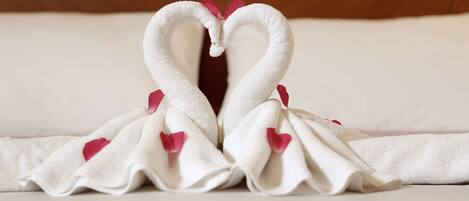 A towel arranged in the shape of two swans with hearts and rose petals.