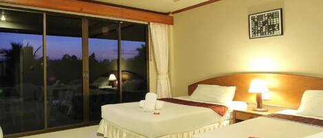 A hotel room with two beds, a large sliding glass door, and a view of the outdoors.