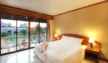 A hotel room with a large bed, two bedside lamps, a nightstand, and a balcony with a view of palm trees and buildings.