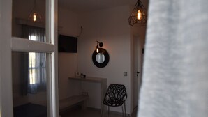 A room with a white bench, a black chair, a wall-mounted TV, and two hanging light fixtures. - Diamantis Studios (Naxos)