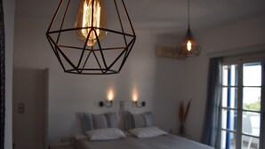 A bedroom with a bed, two wall-mounted lights, and a geometric pendant light. - Diamantis Studios (Naxos)