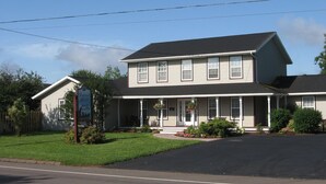 A two-story building with a porch, a signboard, and a well-maintained lawn. - Driftwood Heights Bed & Breakfast (Summerside)