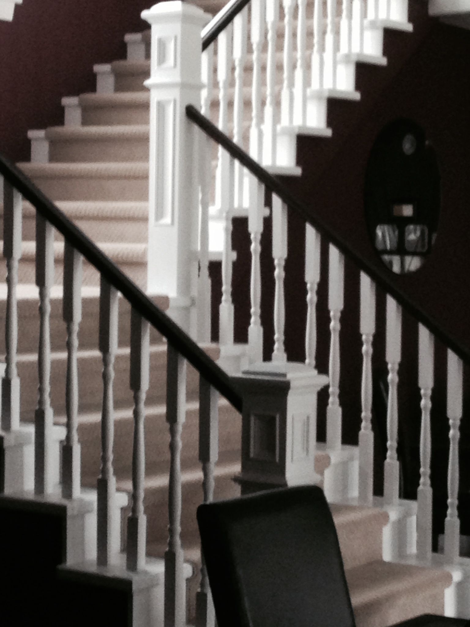 A staircase with white balusters and a black handrail, leading to a landing with a round mirror.