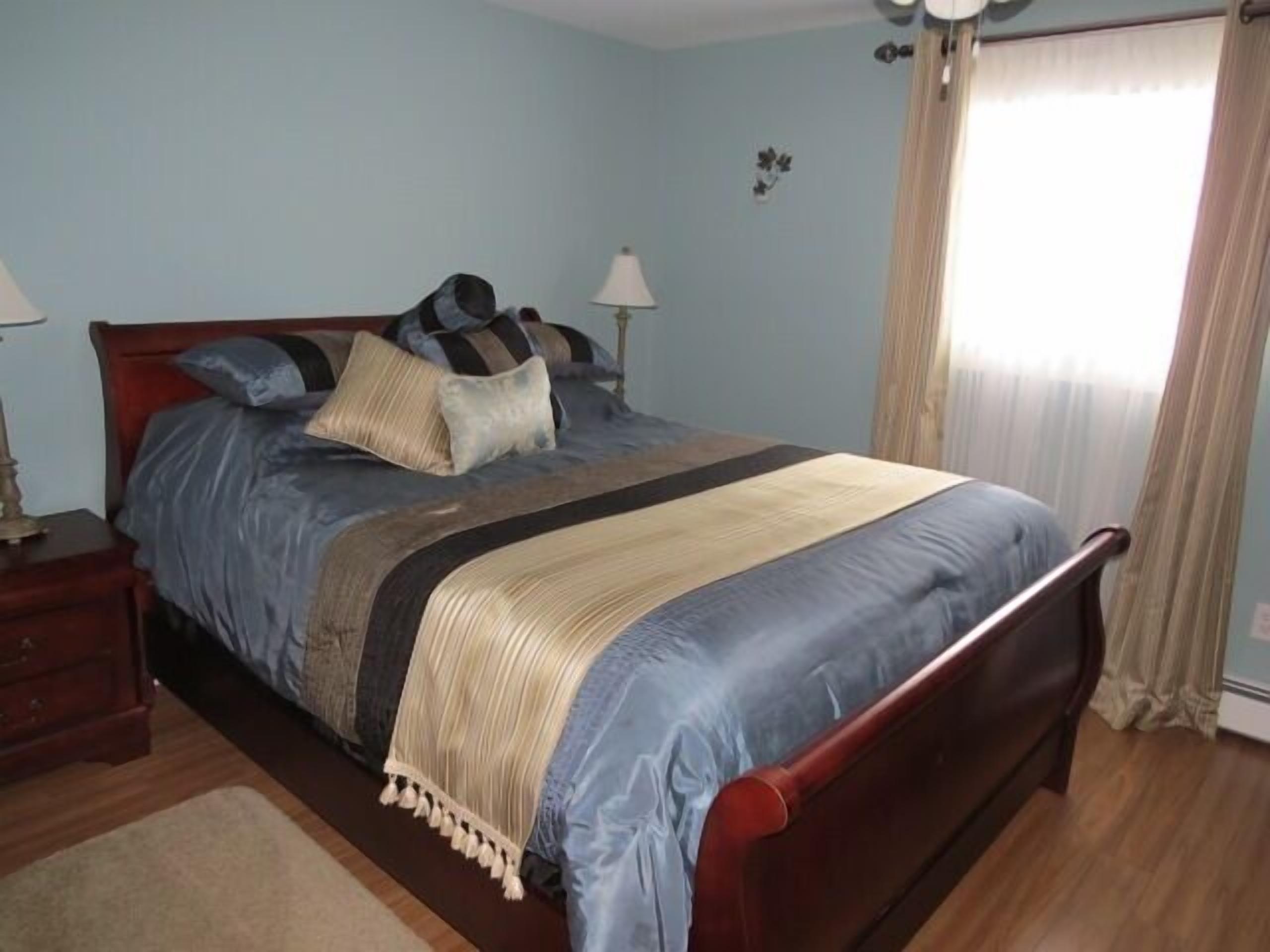 A bedroom with a wooden bed, a nightstand, a lamp, and a window with curtains.