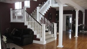 A spacious living room with a wooden staircase and white columns. - Driftwood Heights Bed & Breakfast (Summerside)