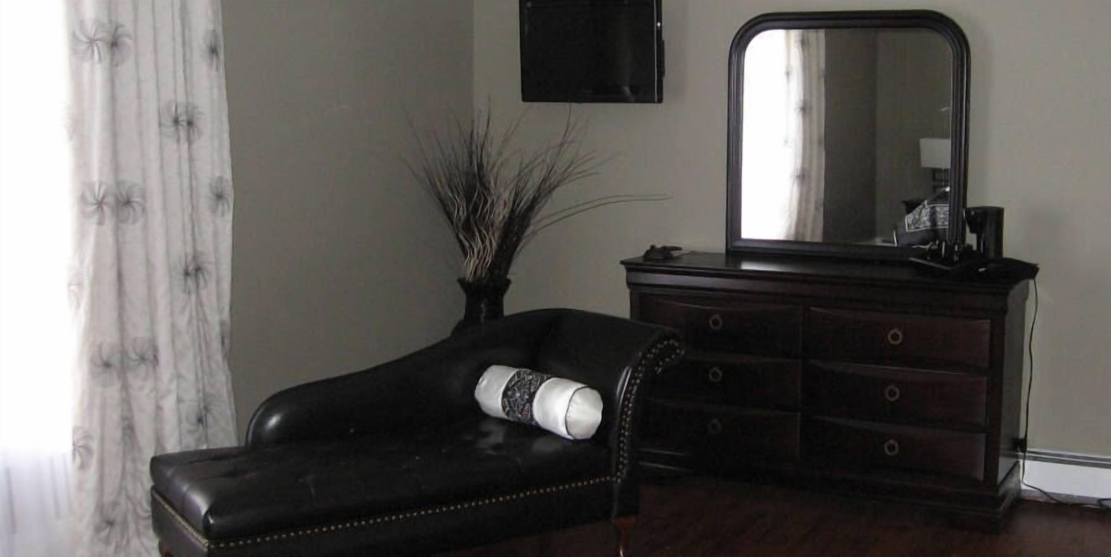 A room with a black leather sofa, a wooden dresser, and a large mirror.