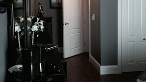 A hallway with a piano, a white door, and a wall-mounted light fixture. - Driftwood Heights Bed & Breakfast (Summerside)