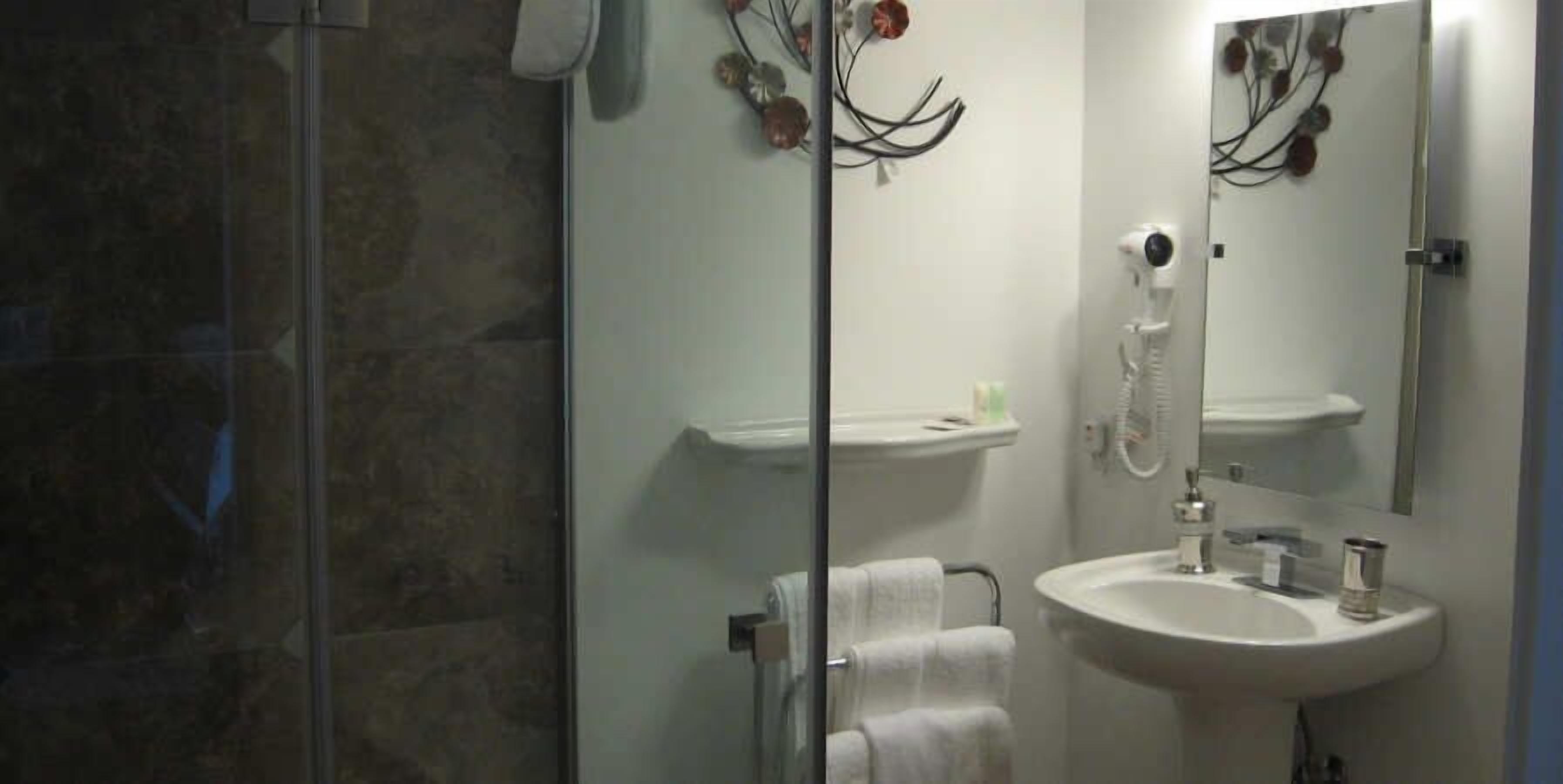 A bathroom with a glass shower enclosure, a sink, and a mirror.