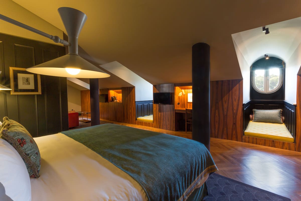 Una habitación amplia con una cama grande, un ventilador de techo, un pequeño rincón de descanso y una ventana.
