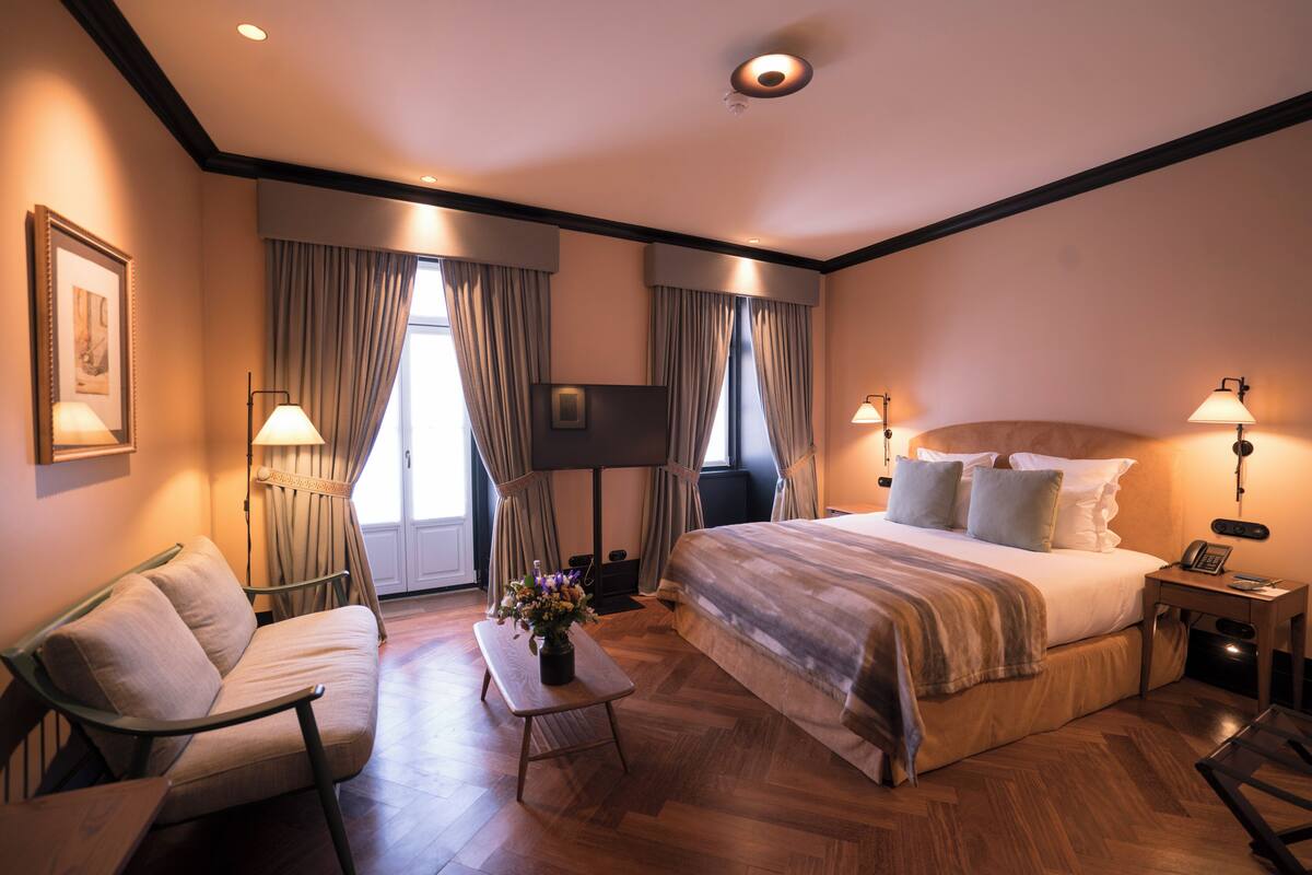 Una habitación de hotel con una cama grande, un sofá, una mesita con un florero y un televisor.