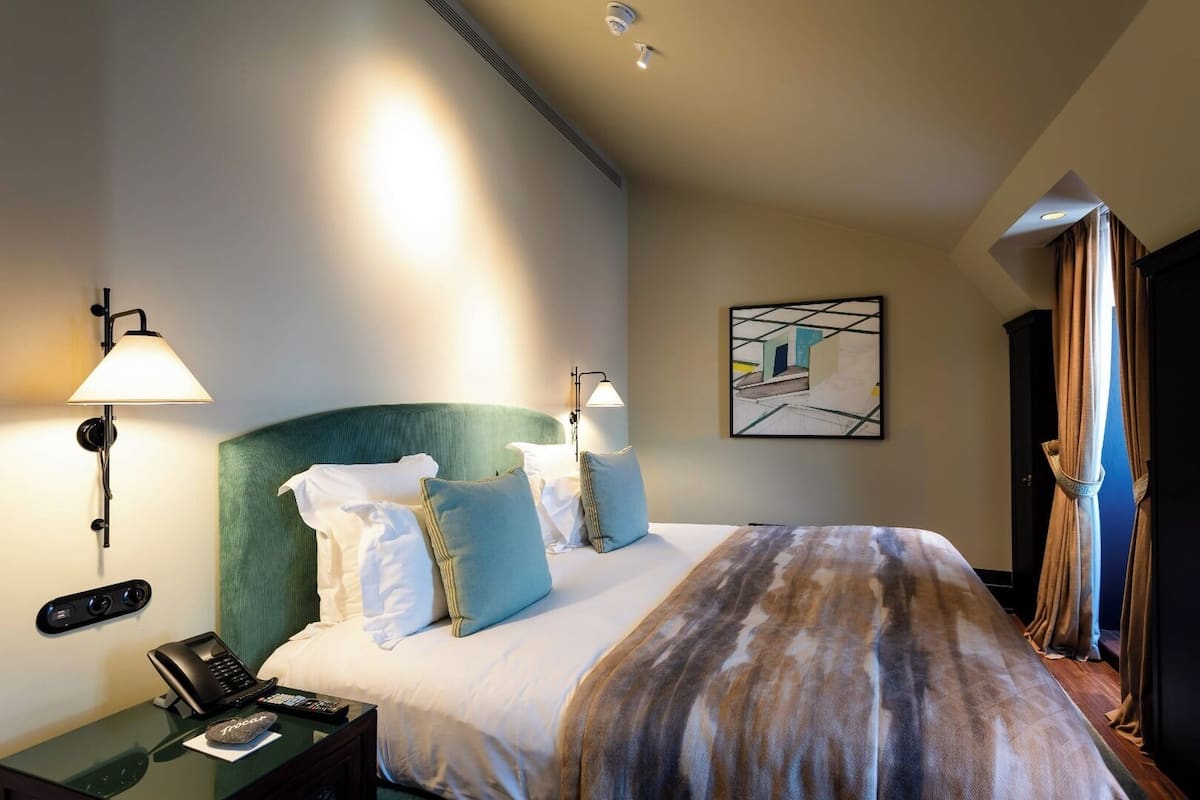 Una habitación de hotel con una cama grande, dos lámparas de noche, un teléfono y un cuadro en la pared.