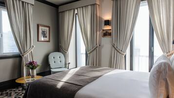 A hotel room with a large bed, a chair, a small table with a vase of flowers, and curtains on the windows.