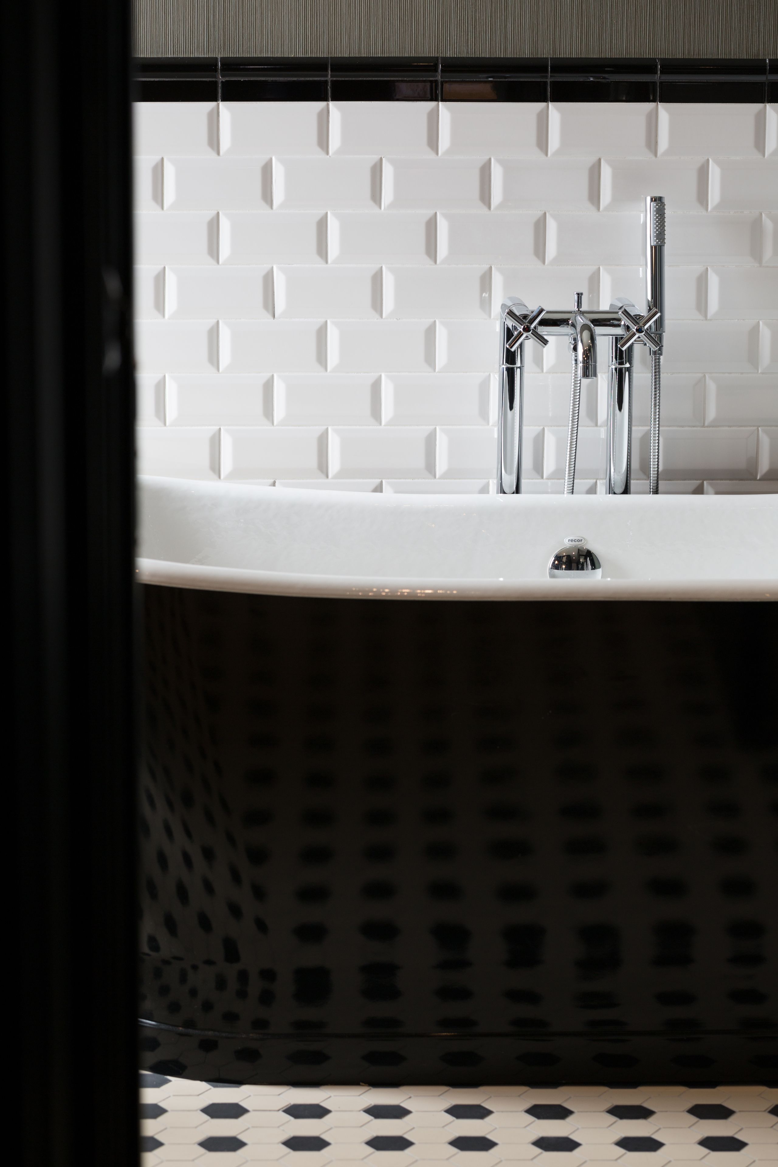 Un baño moderno con pared de azulejos blancos, suelo perforado negro y grifo cromado.