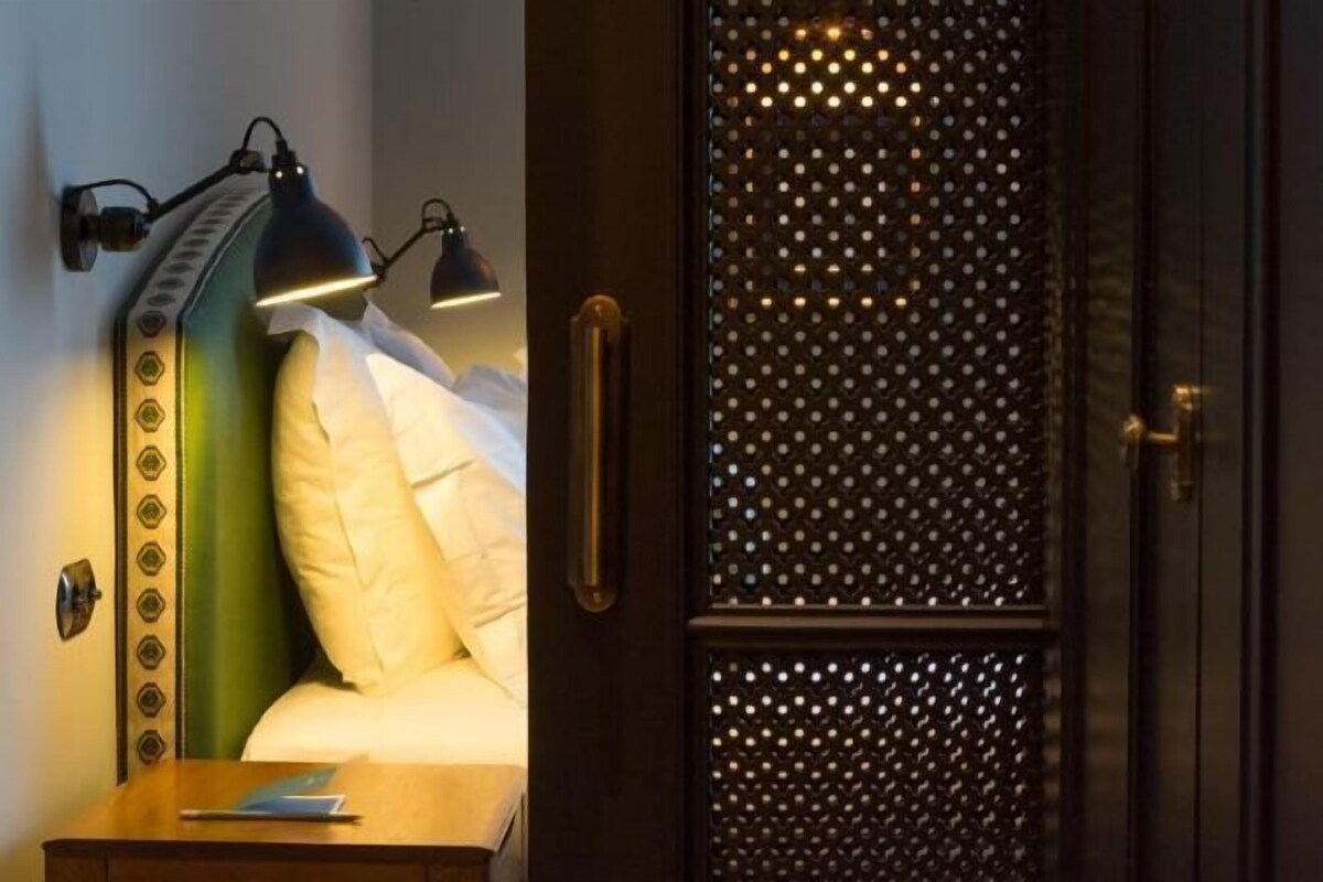 Habitación de hotel con cama, dos lámparas de noche, mesita de noche y un panel decorativo en la pared.