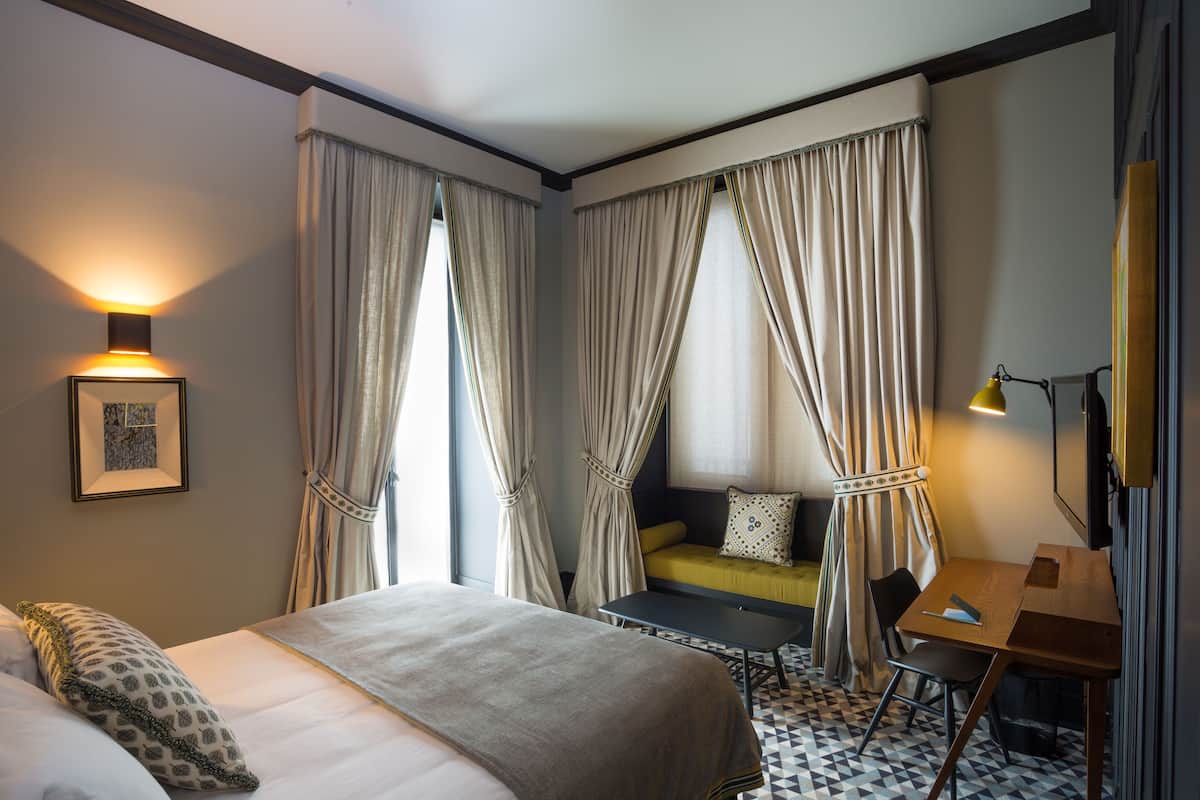 Una habitación de hotel con cama, escritorio, silla, sofá y cortinas.