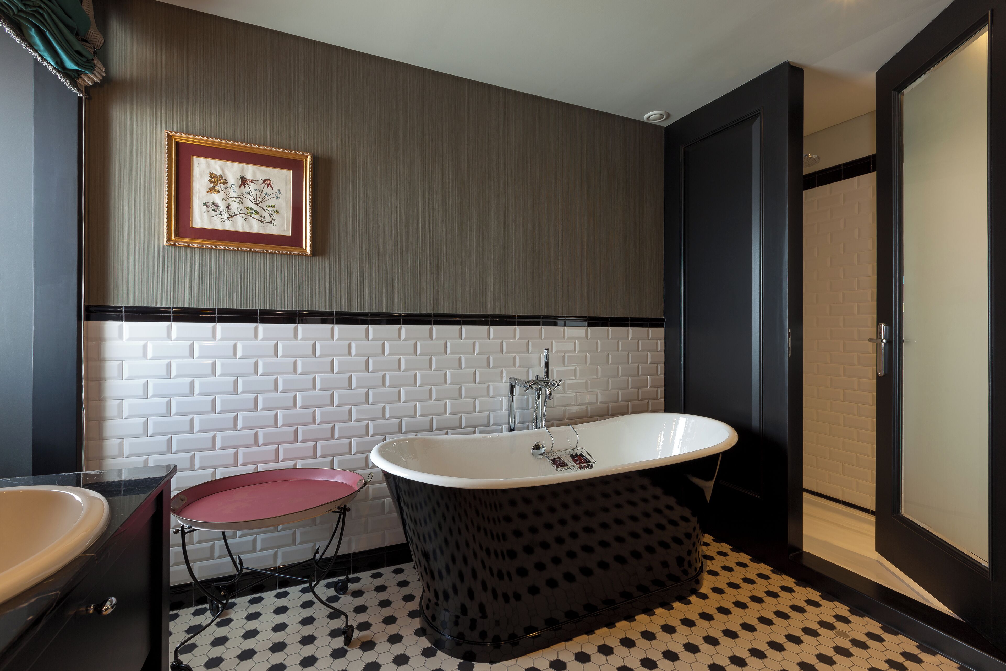 Ein modernes Badezimmer mit einer freistehenden Badewanne, einem kleinen runden Tisch und einer weißen Fliesenwand mit schwarzem Rahmen.