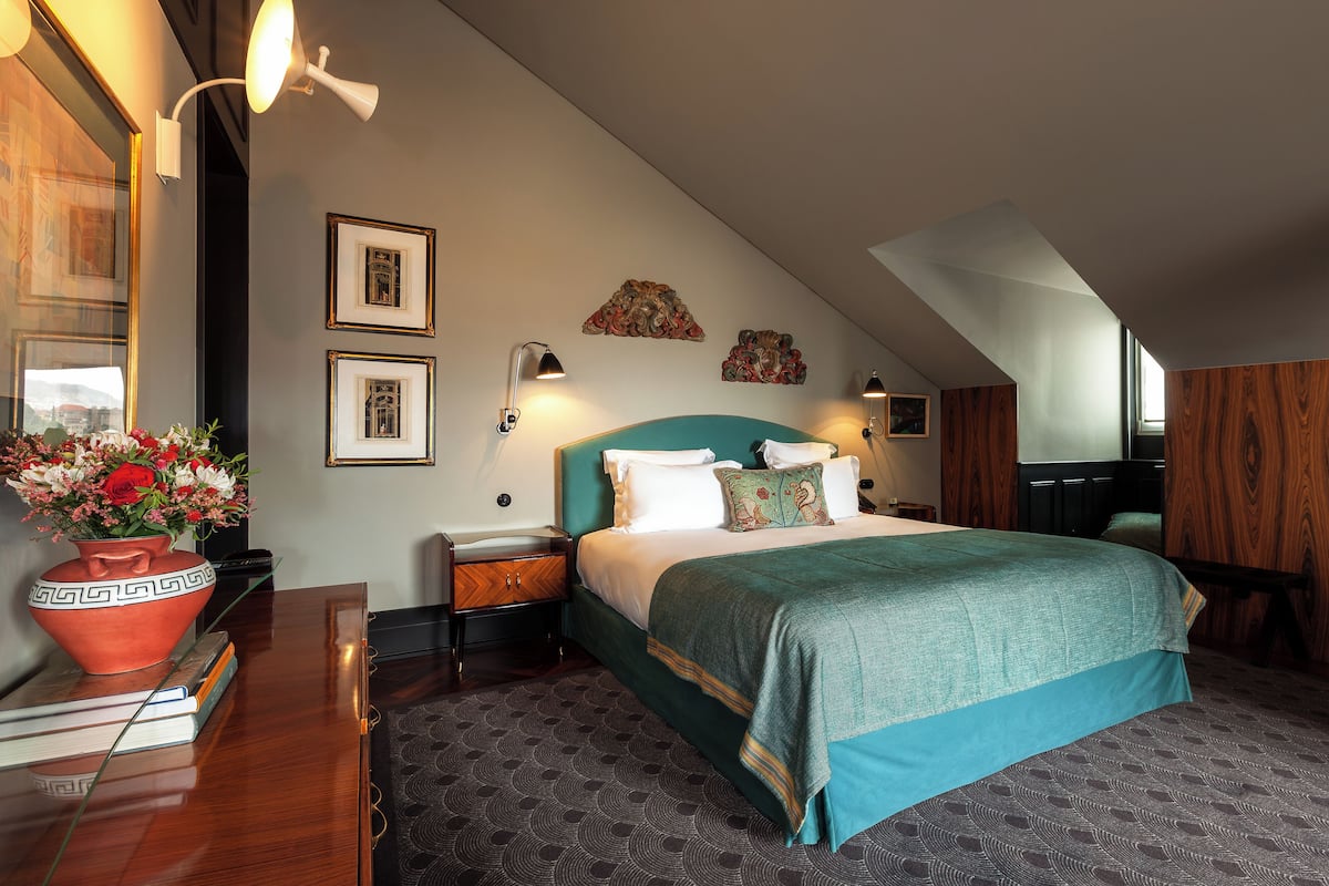 Un dormitorio con una cama grande, una mesita de noche, un jarrón de flores y cuadros en la pared.