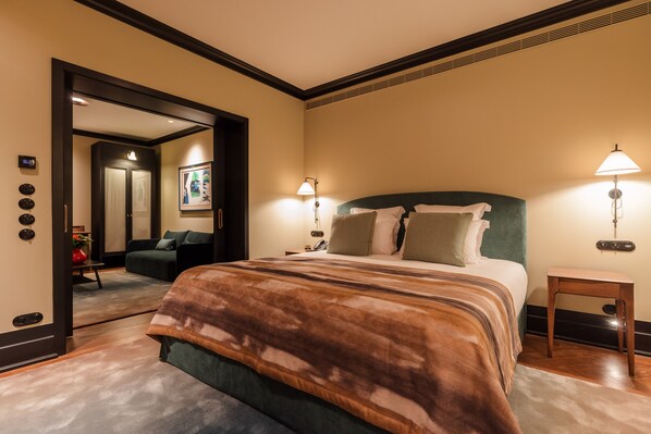 A hotel room with a large bed, a sitting area with a sofa, a small table, and a nightstand with a lamp.