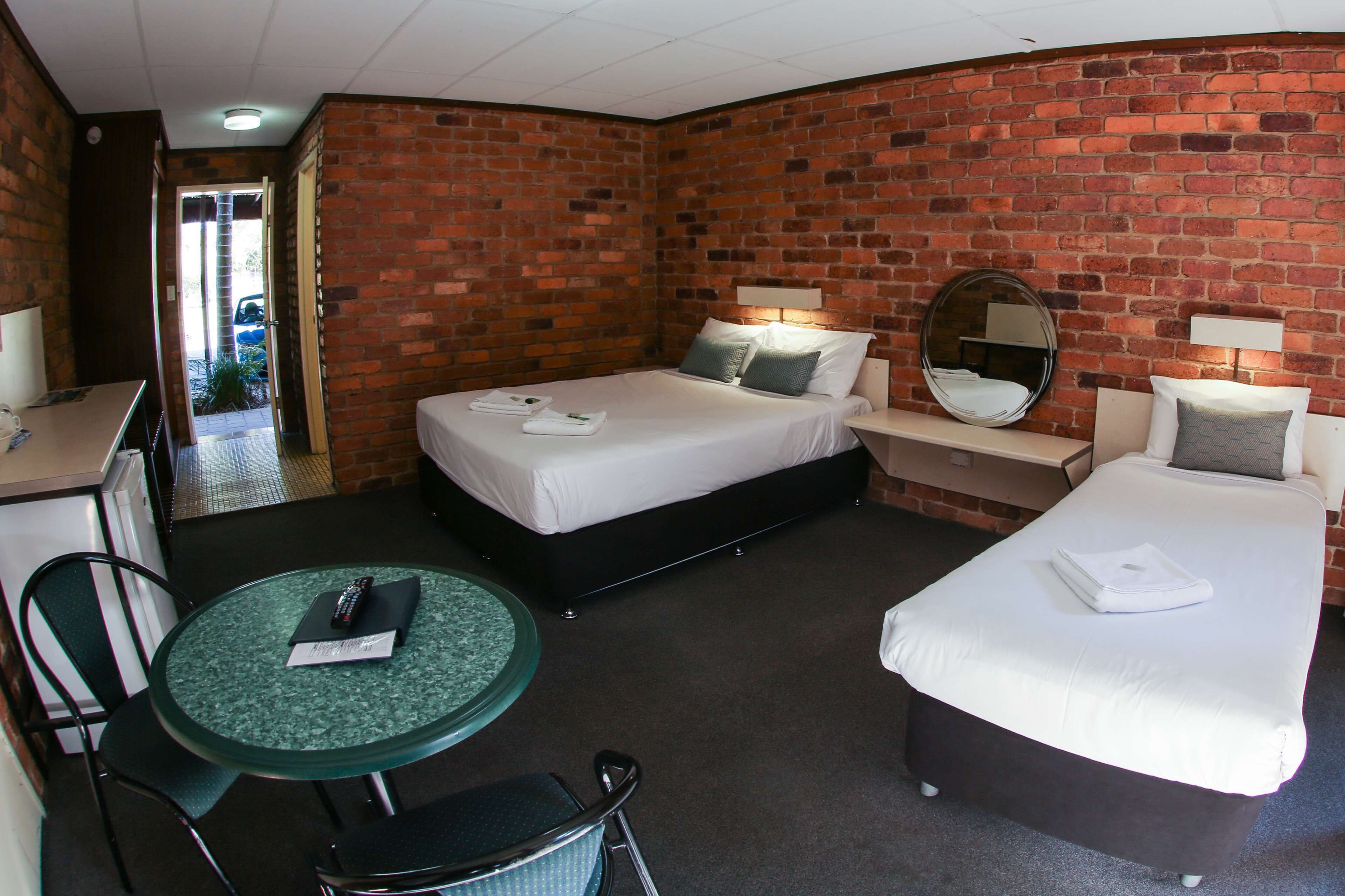 A hotel room with two beds, a desk, a chair, a round table, and a brick wall.