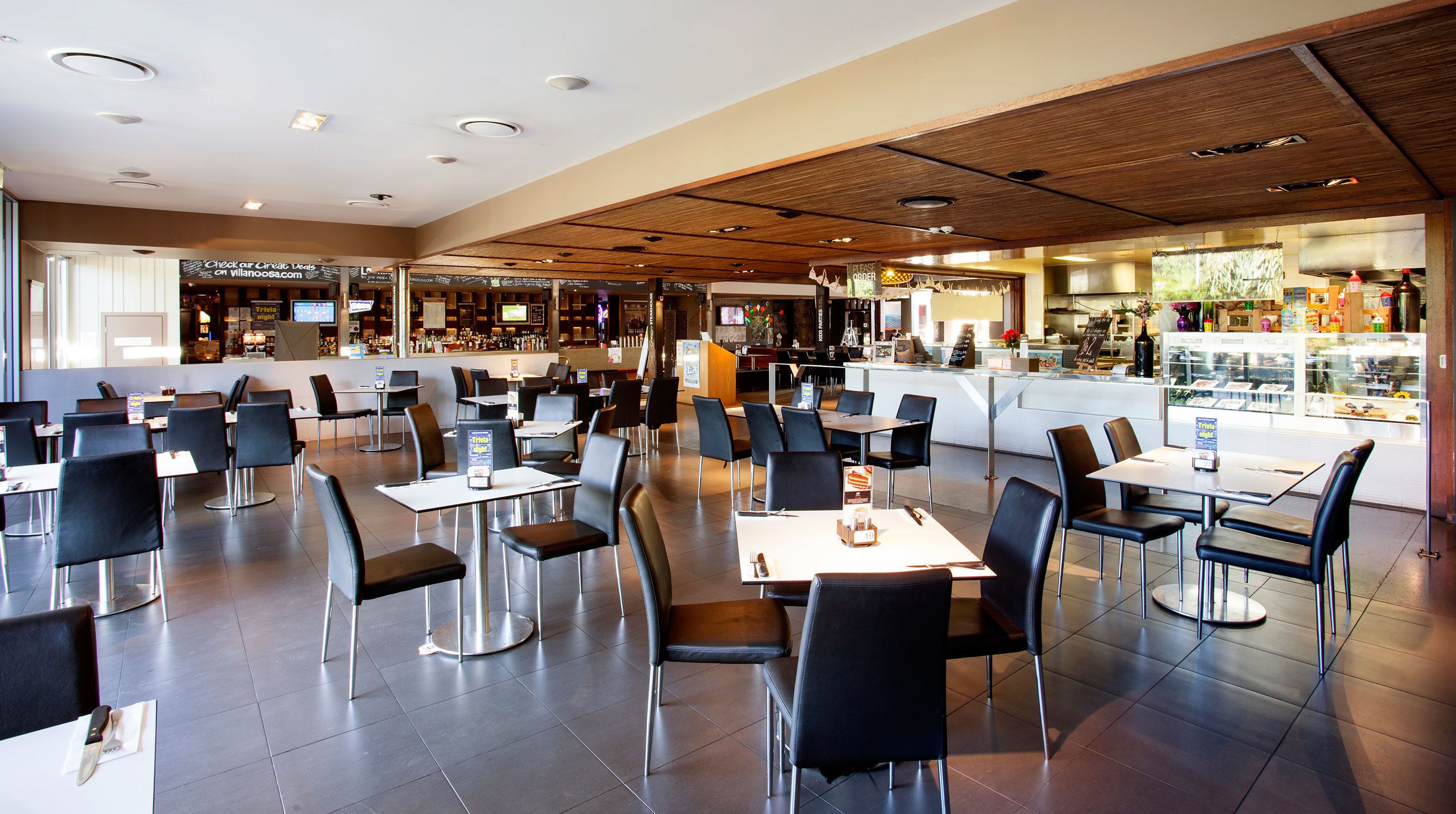 A spacious restaurant with multiple tables and chairs, a counter with a menu, and a bar area.