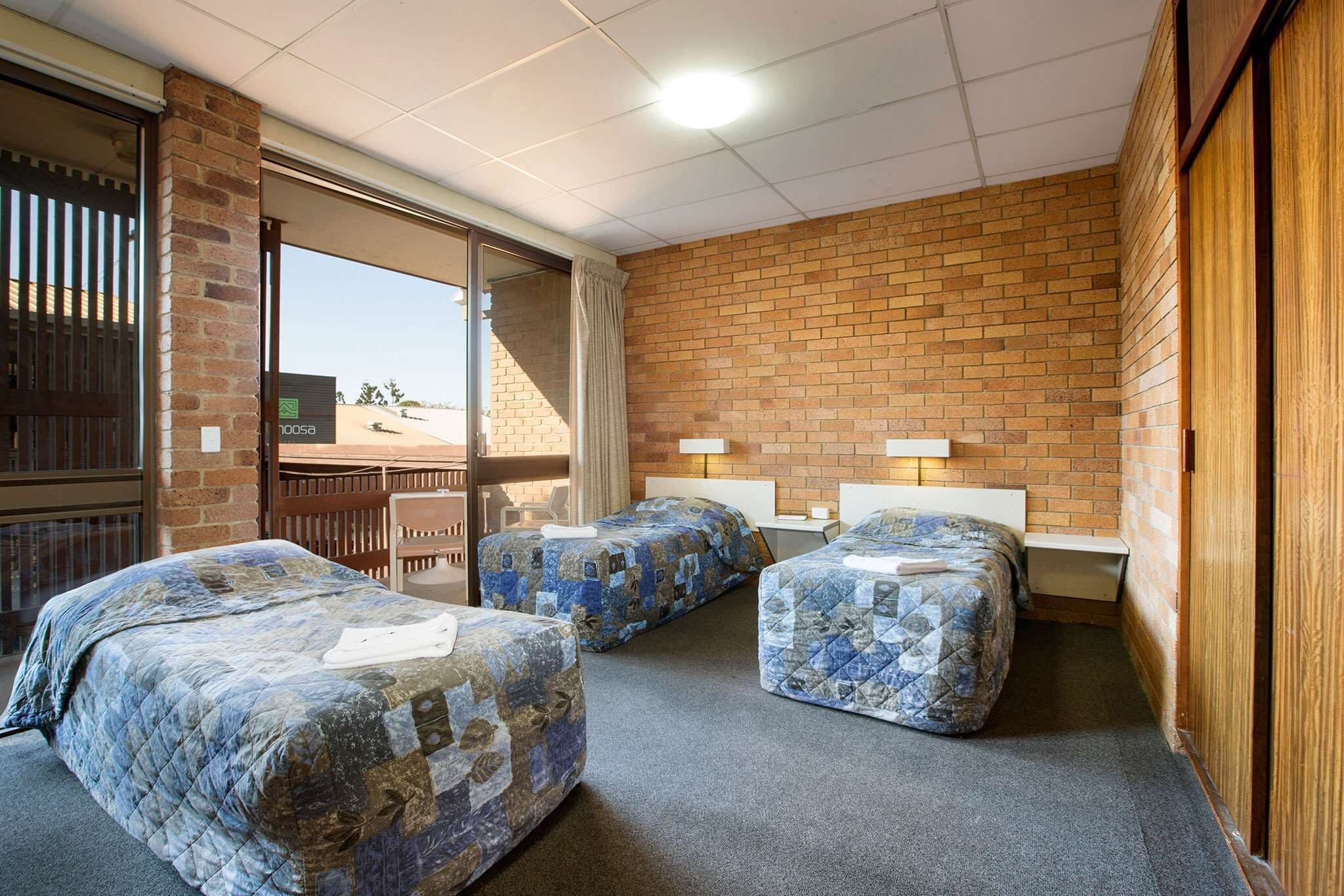 A room with three beds, a brick wall, and a view of the desert.