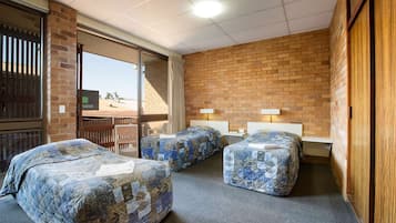A room with three beds, a brick wall, and a view of the desert.