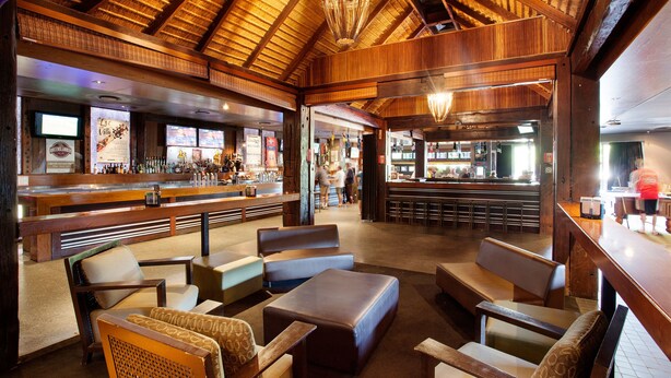 Un intérieur rustique avec des poutres en bois, un coin bar et des espaces aménagés pour s’asseoir.