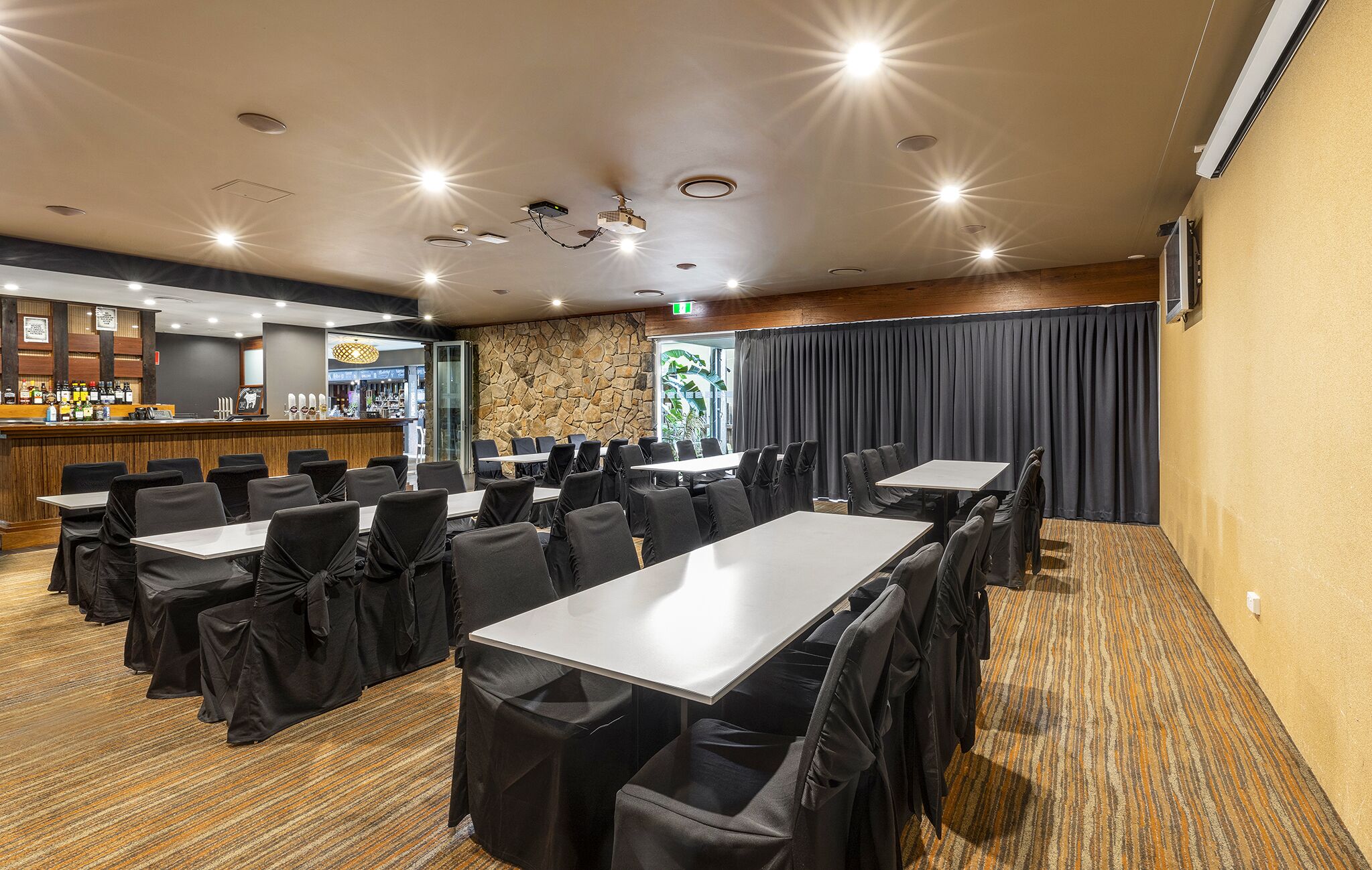 Una sala de conferencias con mesas y sillas, una zona de bar y una pared de piedra.
