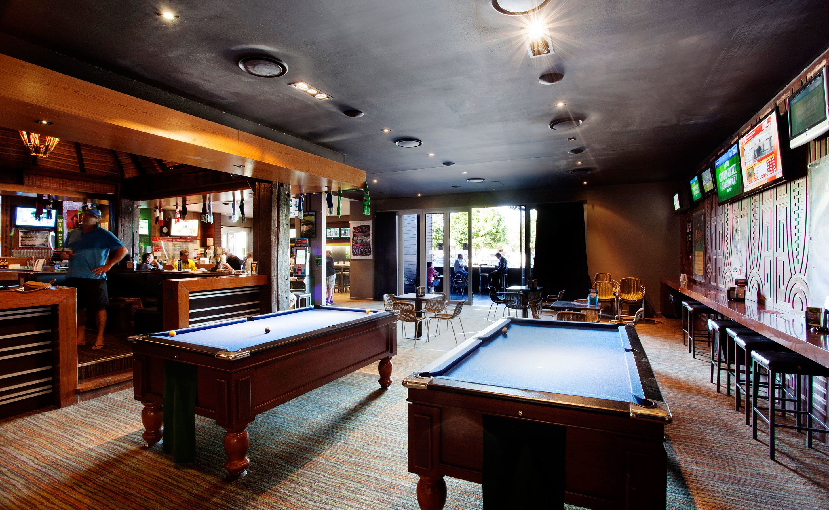A billiards room with pool tables, a bar area, and a seating area with tables and chairs.