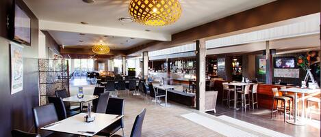 A modern restaurant with a bar area, multiple seating options including tables and booths, and a patterned ceiling design.