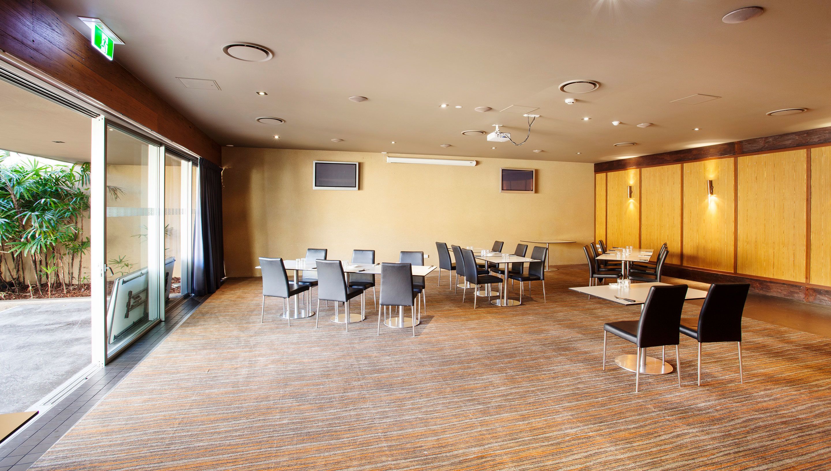 Una sala conferenze con diversi tavoli e sedie, un'ampia finestra con tende e un pannello di parete in legno.