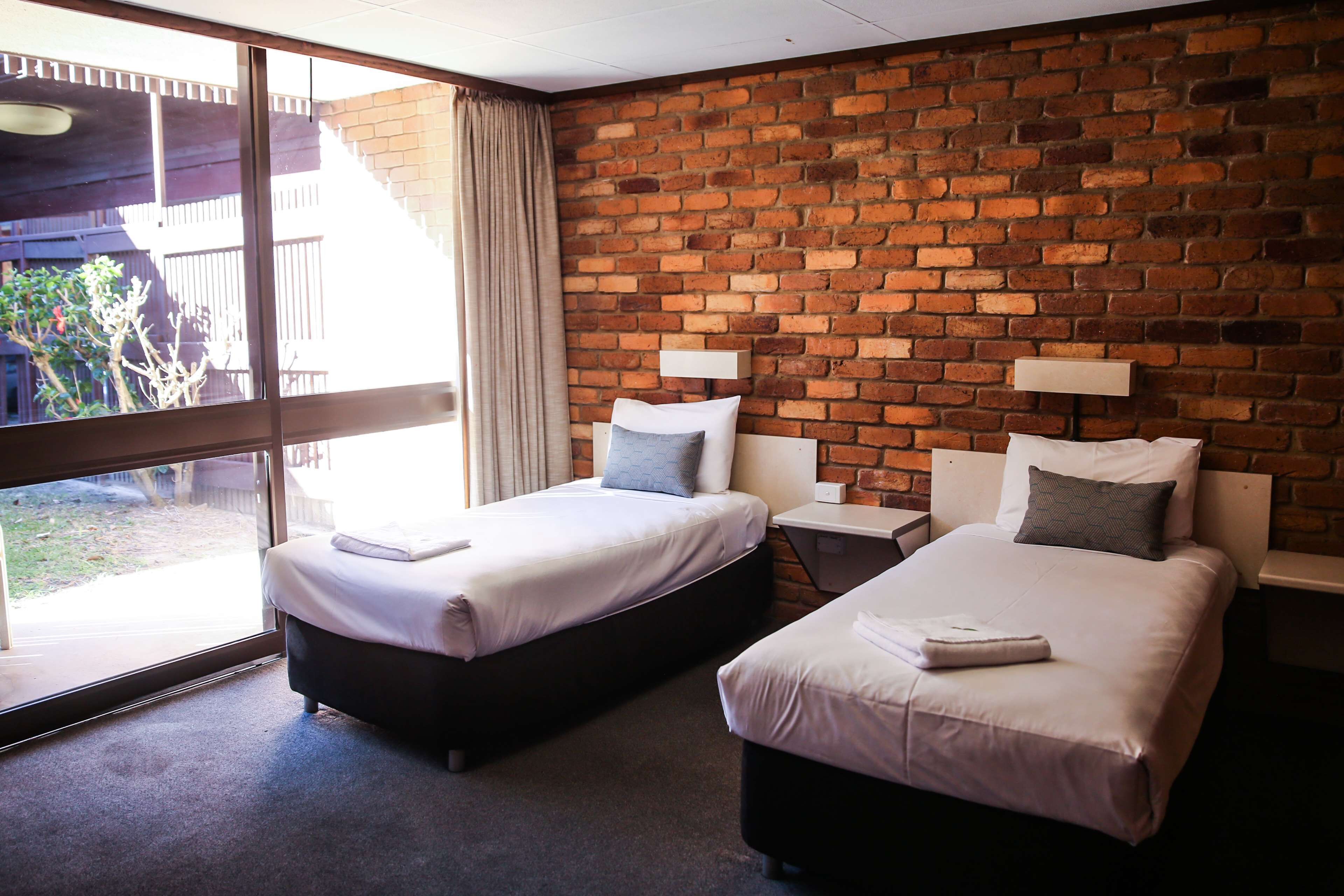 A hotel room with two beds, a brick wall, and a large window.